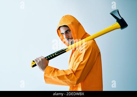 Jeune homme effrayant en imperméable orange tenant une grosse hache arrière-plan blanc Banque D'Images