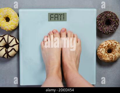 Personne debout sur l'échelle numérique de poids montrant les mots GRAS, et les donuts de nourriture de junk sur le fond, concept de régime Banque D'Images