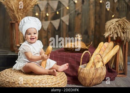 Petit boulanger mignon avec une baguette française dans un intérieur rustique en bois Banque D'Images