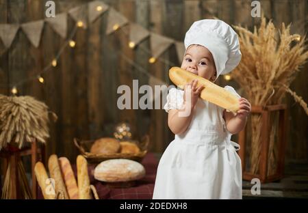 Adorable bébé fille portant un costume de boulanger mangeant du pain long Banque D'Images
