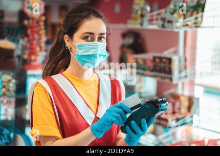 Portrait d'une travailleuse en uniforme avec un masque médical sur son visage, faisant un paiement en ligne par un terminal. Concept de paiements en ligne par ba Banque D'Images