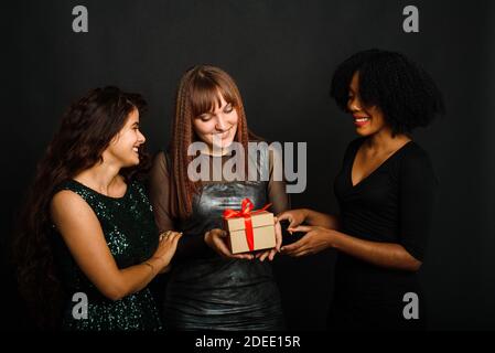 Image de la belle trois jeunes femmes se réjouissant en se tenant avec la boîte actuelle isolée sur fond noir pendant la célébration de noël. Banque D'Images