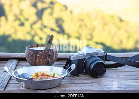 Oeufs frits dans une poêle, riz bouilli en noix de coco et appareil photo sur une table en bois arrière-plan flou vues arbre. Banque D'Images