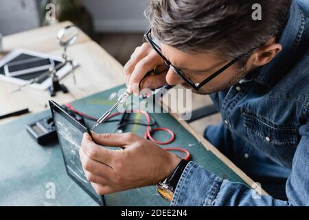 Vue à grand angle du réparateur avec écran cassé à fixation par tournevis de la tablette sur le lieu de travail sur un arrière-plan flou Banque D'Images