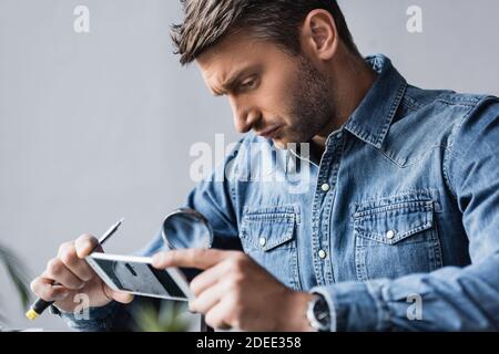 Réparateur concentré regardant à travers la loupe au téléphone portable démonté avec cassé affichage sur un premier plan flou Banque D'Images