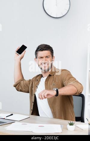 Homme d'affaires en colère regardant l'appareil photo tout en se débarrassant du smartphone sur le lieu de travail Banque D'Images