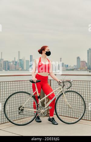 Jeune cycliste portant un masque facial avec un vélo au bord de l'eau Banque D'Images