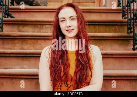 Portrait d'une jeune femme aux cheveux rouges assis à l'extérieur sur un stoop. Banque D'Images