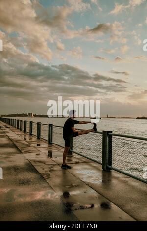 Athlète masculin s'étendant sur le front de mer pendant le coucher du soleil. Banque D'Images