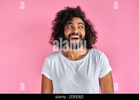 portrait de gai positif homme d'apparence arabe regardant loin rire, il écoute blague, s'amuser avec quelqu'un, isolé sur fond rose Banque D'Images