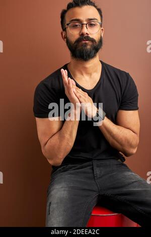 beau arabe mâle posant à la caméra tout en étant assis sur le canon en studio. course mixte cool mâle regarde avec confiance la caméra, modèle Banque D'Images