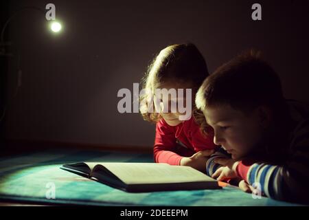 Deux frères et sœurs heureux lisant le livre à l'obscurité avec la lampe de poche à cacher la place sous le lit Banque D'Images