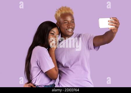 Positif noir gars prenant selfie avec sa chère amie sur smartphone sur fond de studio lilas Banque D'Images