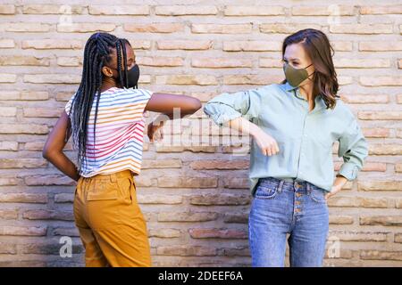 Les jeunes femmes multiethniques portant des masques saluent les unes les autres leurs coudes Banque D'Images