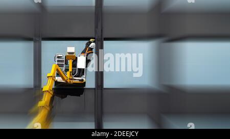 Homme nettoyant nettoyage vitre windows sur haut bâtiment moderne dans l'air sur une plate-forme de levage. Polissage du verre employé dans l'air élevée Banque D'Images