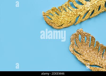 Ornements dorés - feuilles tropicales exotiques sur fond bleu pastel avec espace publicitaire. Flat lay, concept de fête minimaliste. Concept de bijoux créatifs, selec Banque D'Images