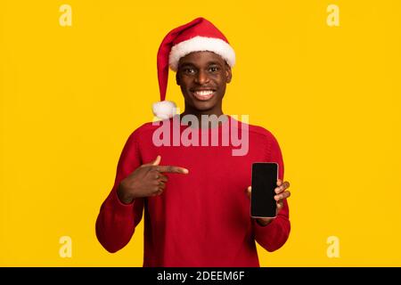 Un homme africain positif à Santa Hat pointant vers un smartphone avec Écran noir Banque D'Images