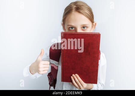 petite fille mignonne est une écolière, pointant vers le livre, fond blanc, publicité, Banque D'Images