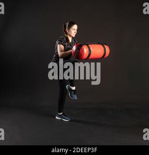 Une fille de forme physique avec un sac d'eau, tire la chaussette, fait des exercices. Sport sur fond noir souriant Banque D'Images