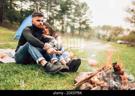 Couple pensif dans la nature torréfaction des guimauves sur feu de camp Banque D'Images