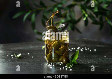 Câpres. Câpres en conserve marinées ou marinées fruits gros plan dans un pot en verre sur fond de table de cuisine grise. Copier l'espace Banque D'Images