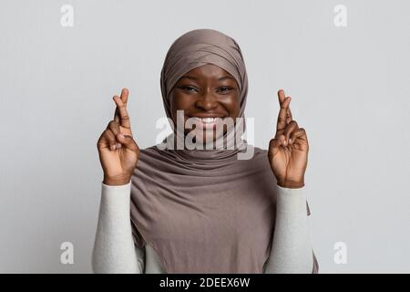 Veuillez, s'il vous plaît, s'il vous plaît. Closeup portrait of dreamy black jeune musulmane en hijab crossing fingers, rendant le souhaitent, sur fond jaune Banque D'Images