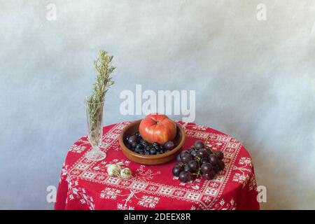 Reste la vie d'un bol en faïence rempli de fruits, légumes, noix sur une table recouverte d'une nappe rouge ornée de décorations de Noël et de romarin. Banque D'Images