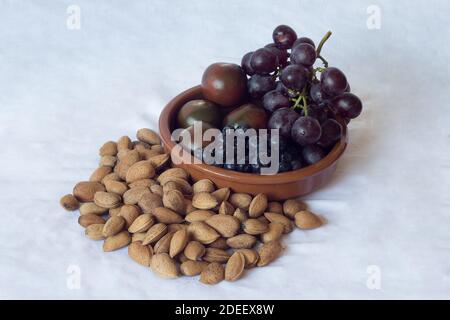 Simple encore sur toile vintage composé d'amandes décortiquées et d'un bol en argile fait main rempli de tomates, de bleuets et de raisins noirs. Banque D'Images