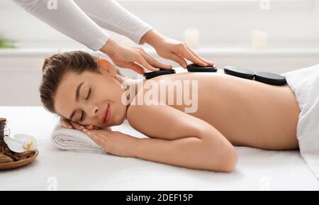 Masseuse méconnue mettant des pierres noires sur le dos de la jeune femme Banque D'Images