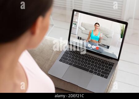Femme ayant un appel vidéo avec un instructeur de fitness sur un ordinateur portable intérieur Banque D'Images