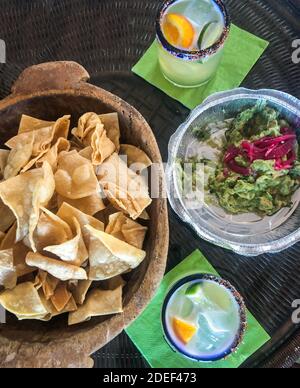 Plats mexicains à emporter. Guacamole à emporter dans un récipient à emporter et frites dans un bol en bois avec 2 margaritas dans des verres aux bords sals. ID DE COMPTE. Banque D'Images