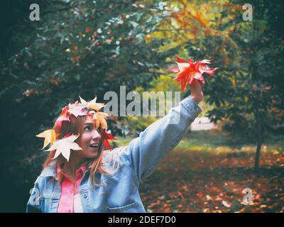 Une fille avec une tête décorée de feuilles d'érable rouges contient un bouquet de feuilles d'automne dans un parc sa main levée Banque D'Images