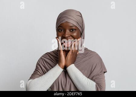 Surprise la femme noire dans hijab touchant le visage dans l'excitation, regardant la caméra Banque D'Images