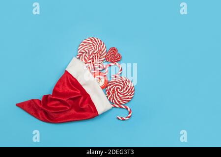 Tas de bonbons dans un chapeau du Père Noël. Cannes de Noël rouges et sucettes sur fond bleu. Bonbons de Noël joyeux et concept bonne année Banque D'Images