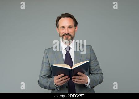 Happy School enseignant en costume formel tenir livre ouvert enseignement leçon fond gris, littérature. Banque D'Images