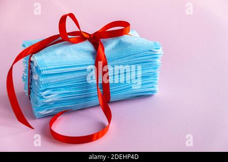 Masques médicaux de protection comme cadeau, attaché avec un ruban rouge, sur un fond rose. Concept de pandémie de coronavirus. Mise au point sélective. Copier l'espace. Banque D'Images