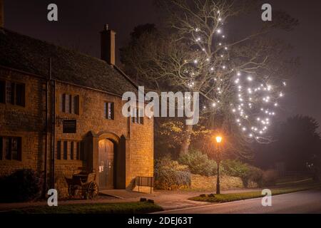 Le musée de Broadway et les décorations de lumière d'arbre de Noël la nuit dans la brume. Broadway, Cotswolds, Worcestershire, Angleterre Banque D'Images