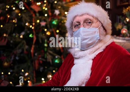 Le Père Noël en masque médical. Portrait positif Santa assis près de l'arbre de Noël. Bonne année Covid 2021 Banque D'Images