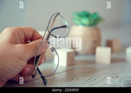 Une main mâle tient des lunettes à rebord fin et repose sur une table en bois. Banque D'Images