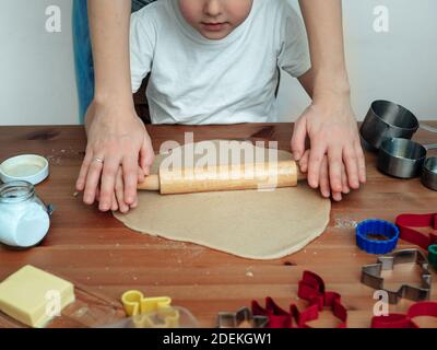 Jeune mère et fils faisant des biscuits de noël. Image rognée mains de mère et de fils pétrissant la pâte ensemble. Préparation de Noël à la cuisson. Mère enseignant à son fils comment faire rouler la pâte avec la goupille élastique Banque D'Images