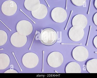 Crème hydratante en pot en verre ouvert, tampons de coton et bâtonnets de coton sur fond violet clair texturé. Vue de dessus. Bio bio naturel bio bio éco soin de la peau bea Banque D'Images