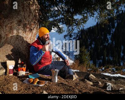 Un touriste boit du café à l'arrêt en hiver dans les montagnes. Faire du café lors d'une randonnée Banque D'Images