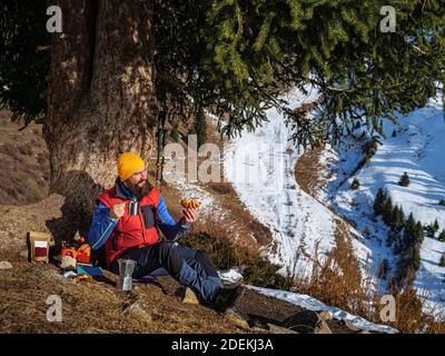 Un touriste mâle barbu boit du café en hiver dans les montagnes. Faire du café lors d'une randonnée. Journée ensoleillée dans les montagnes d'hiver Banque D'Images