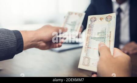 Un homme d'affaires donnant de l'argent de billet de banque des Émirats arabes Unis Dirhams sur une table en bois dans la vie privée - prêt, paiement et le concept de corruption Banque D'Images