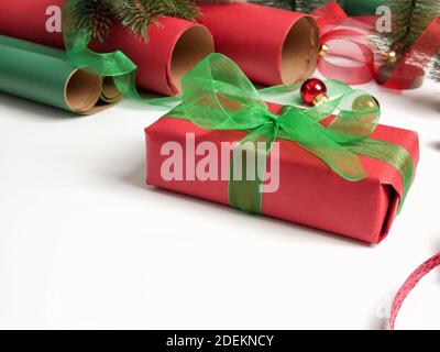 Boîtes-cadeaux, rouleaux de papier rouge et vert, décorations et décorations pour arbres de Noël sur table blanche. Préparation pour les vacances. Vue de dessus, espace de copie. Banque D'Images