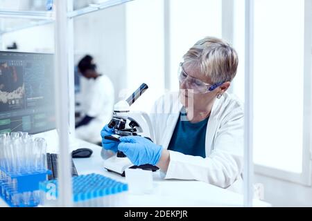 Un scientifique expérimenté pose une lame de verre sur un microscope au cours d'une enquête médicale. Chercheur âgé effectuant des recherches scientifiques dans un laboratoire stérile utilisant une technologie moderne. Banque D'Images