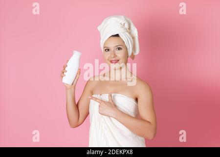 gros plan d'une jeune femme dans une serviette tenir une bouteille blanche de shampooing ou de crème sans un étiquetez-la et pointez-la avec son index Banque D'Images