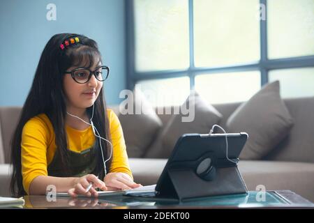 Jeune fille dans des lunettes faisant son travail tout en assistant en ligne classe devant une tablette Banque D'Images