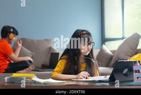 Jeune fille assistant à la classe en ligne avec son frère assis sur La table en arrière-plan pendant le verrouillage Banque D'Images