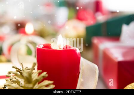 Bougie de cire rouge illuminée avec ruban doré et pin Cone sur fond flou de cadeaux de Noël colorés pour célébrer fêtes de fin d'année Banque D'Images
